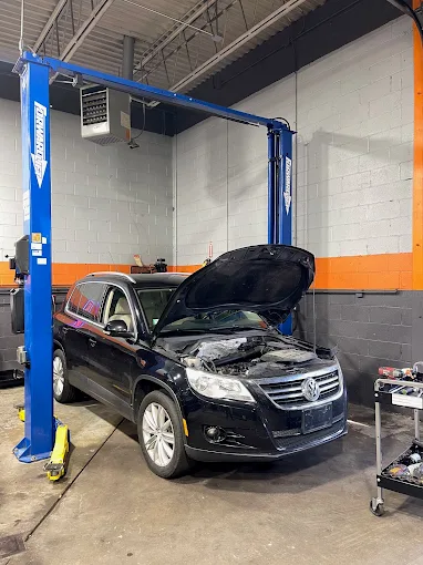 Technician servicing a vehicle engine on a lift at Quiroz Auto Center